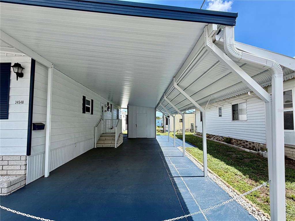 A covered carport with a concrete floor sits between two white mobile homes — 34548 VIOLET DRIVE N, PINELLAS PARK, FL
