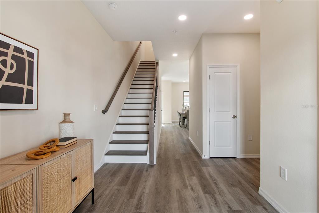 A bright entryway features wood-look flooring, a staircase with a wooden handrail, and a closed door — 4348 CAMBIO GARDENS COURT, TAMPA, FL