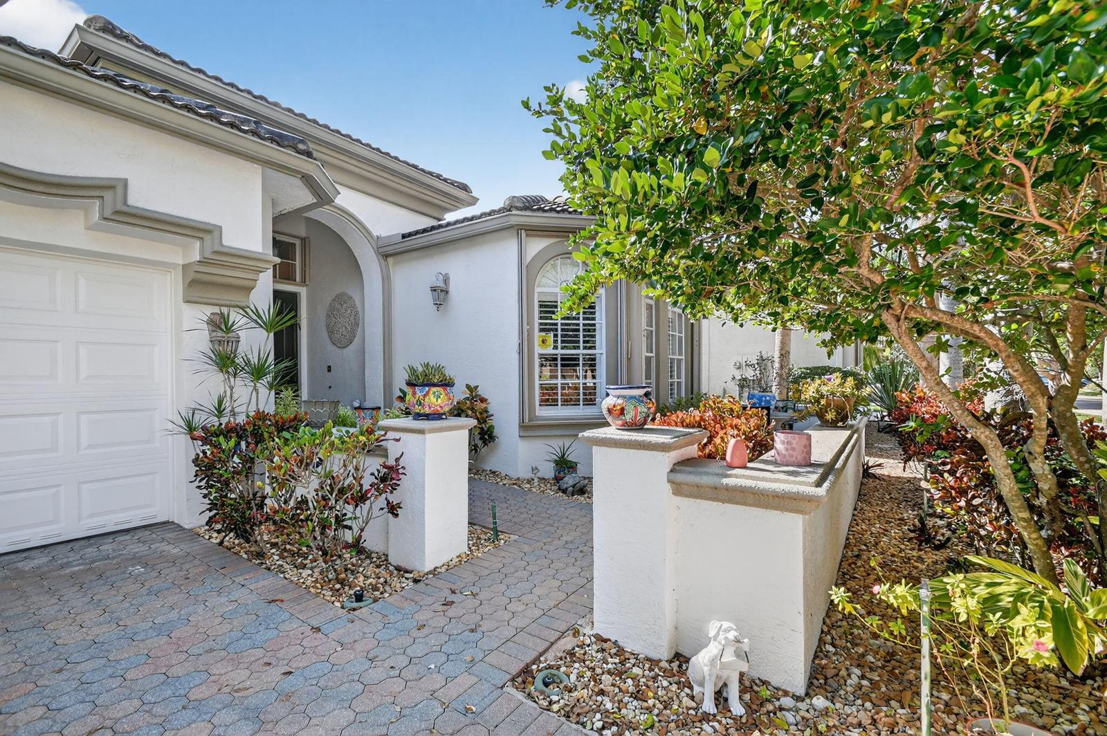 A paved walkway leads to the arched entryway of a white stucco house with double doors — 9842 Via Elegante, Wellington FL 33411, WELLINGTON, FL
