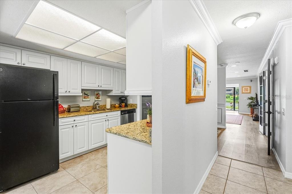 A kitchen with white cabinets, granite countertops, and a black refrigerator opens to a hallway — 4540 BEE RIDGE ROAD UNIT Villa 1, SARASOTA, FL