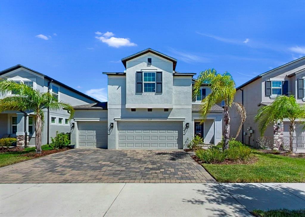 A two-story suburban house with a paver driveway, a three-car garage, and palm trees — 3139 MARINE GRASS DRIVE, WIMAUMA, FL