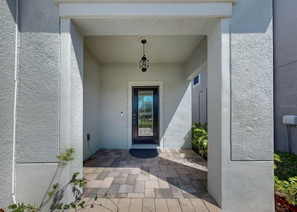 A covered entryway features a paved floor, a dark front door, and a hanging lantern — 3139 MARINE GRASS DRIVE, WIMAUMA, FL