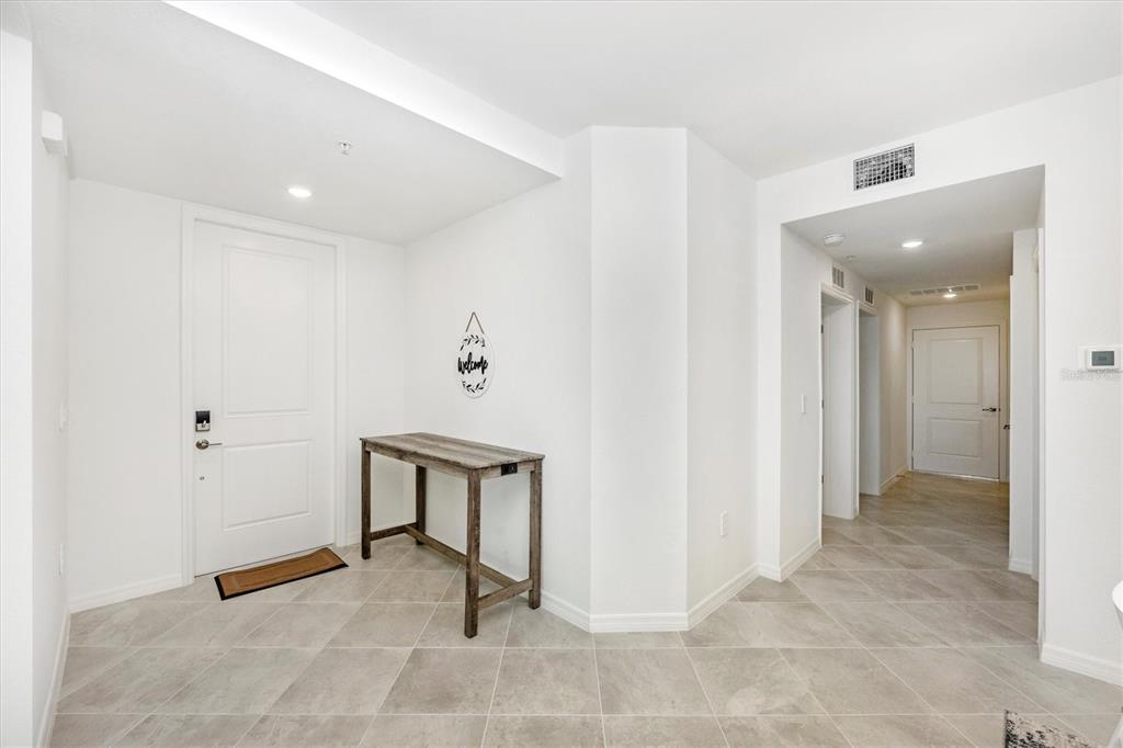 A bright entryway features white walls, tile flooring, a wooden console table, and two doors — 17775 BORACAY COURT UNIT 102, VENICE, FL