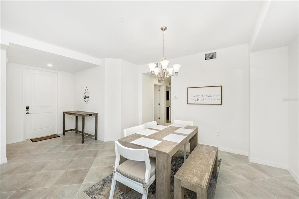 A dining area features a wooden table with chairs and a bench under a chandelier — 17775 BORACAY COURT UNIT 102, VENICE, FL