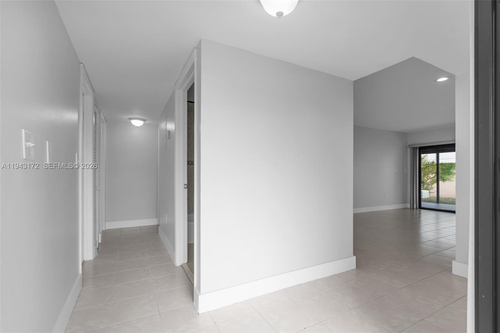 A hallway with light-colored tile flooring leads toward a living area with sliding glass doors — 3815 SW 82nd Ave # 41, Miami FL 33155, MIAMI, FL