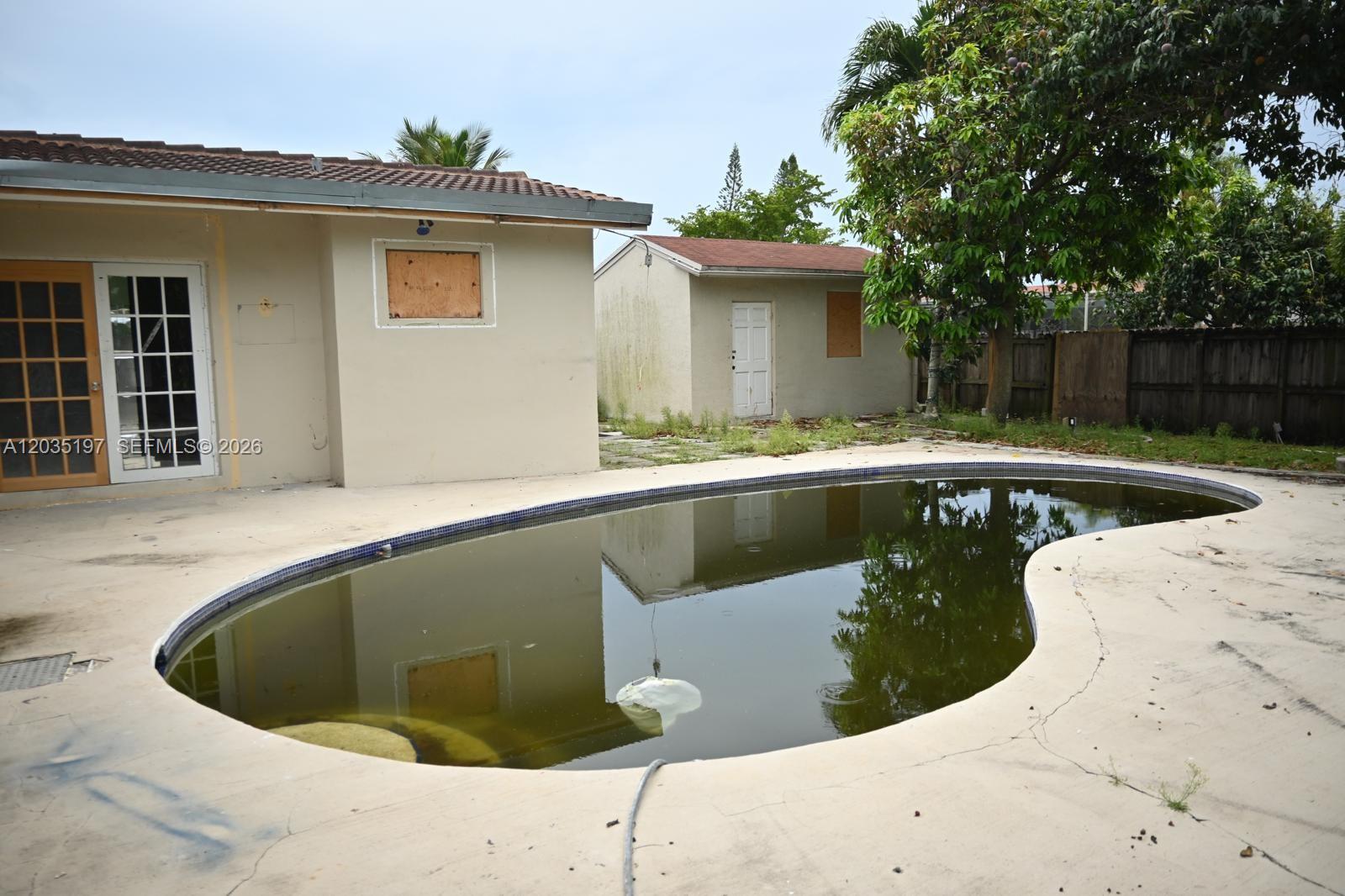 A backyard features a kidney-shaped pool with murky water, a patio, and a detached shed — HOLLYWOOD, FL