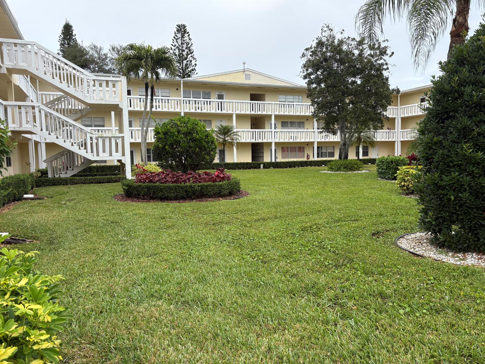 A three-story apartment building with exterior staircases overlooks a landscaped courtyard with green lawn — 186 Dorset E, Boca Raton FL 33434, BOCA RATON, FL