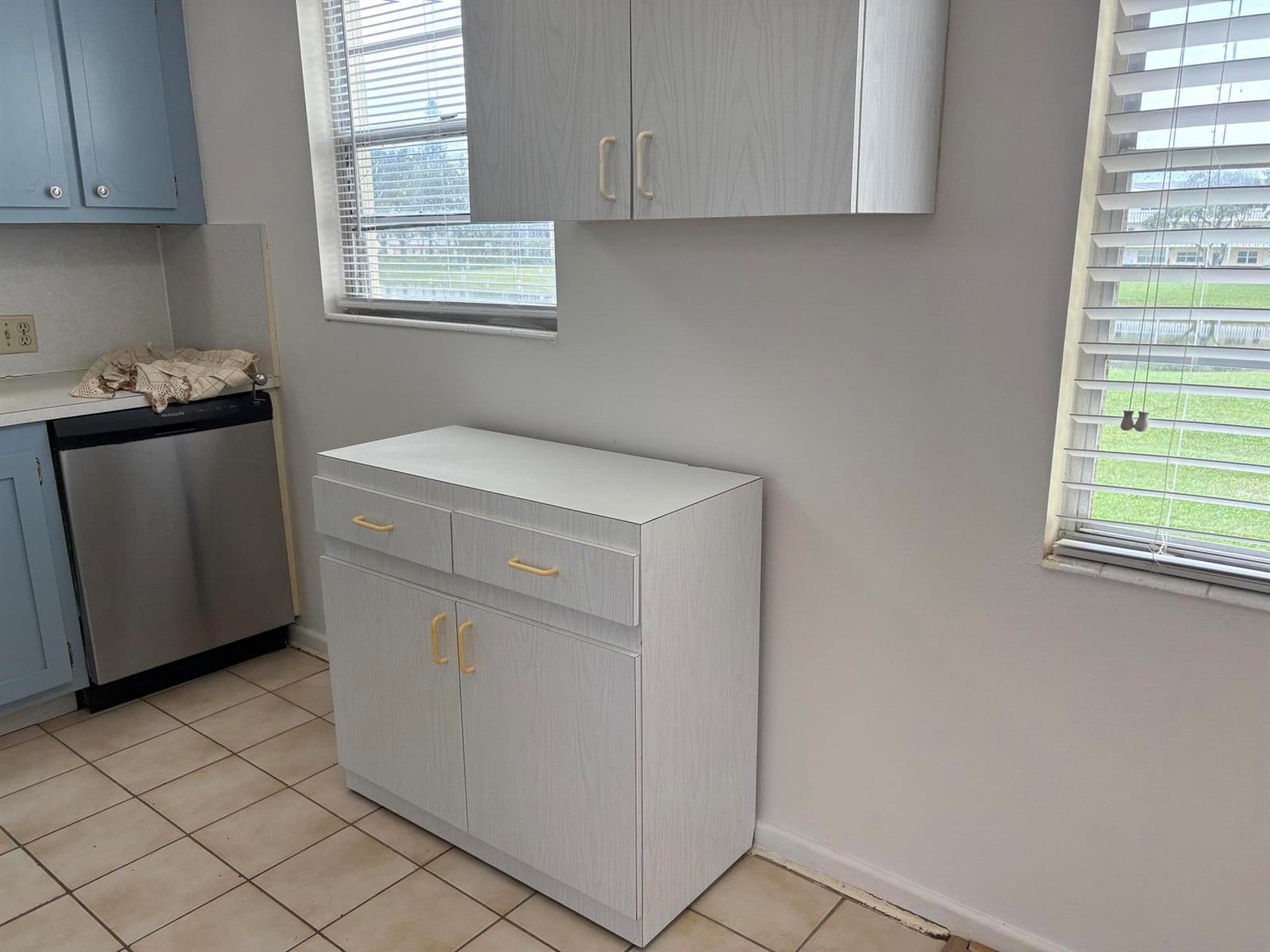 A kitchen features light wood-grain cabinets, a stainless steel dishwasher, and tile flooring — 186 Dorset E, Boca Raton FL 33434, BOCA RATON, FL