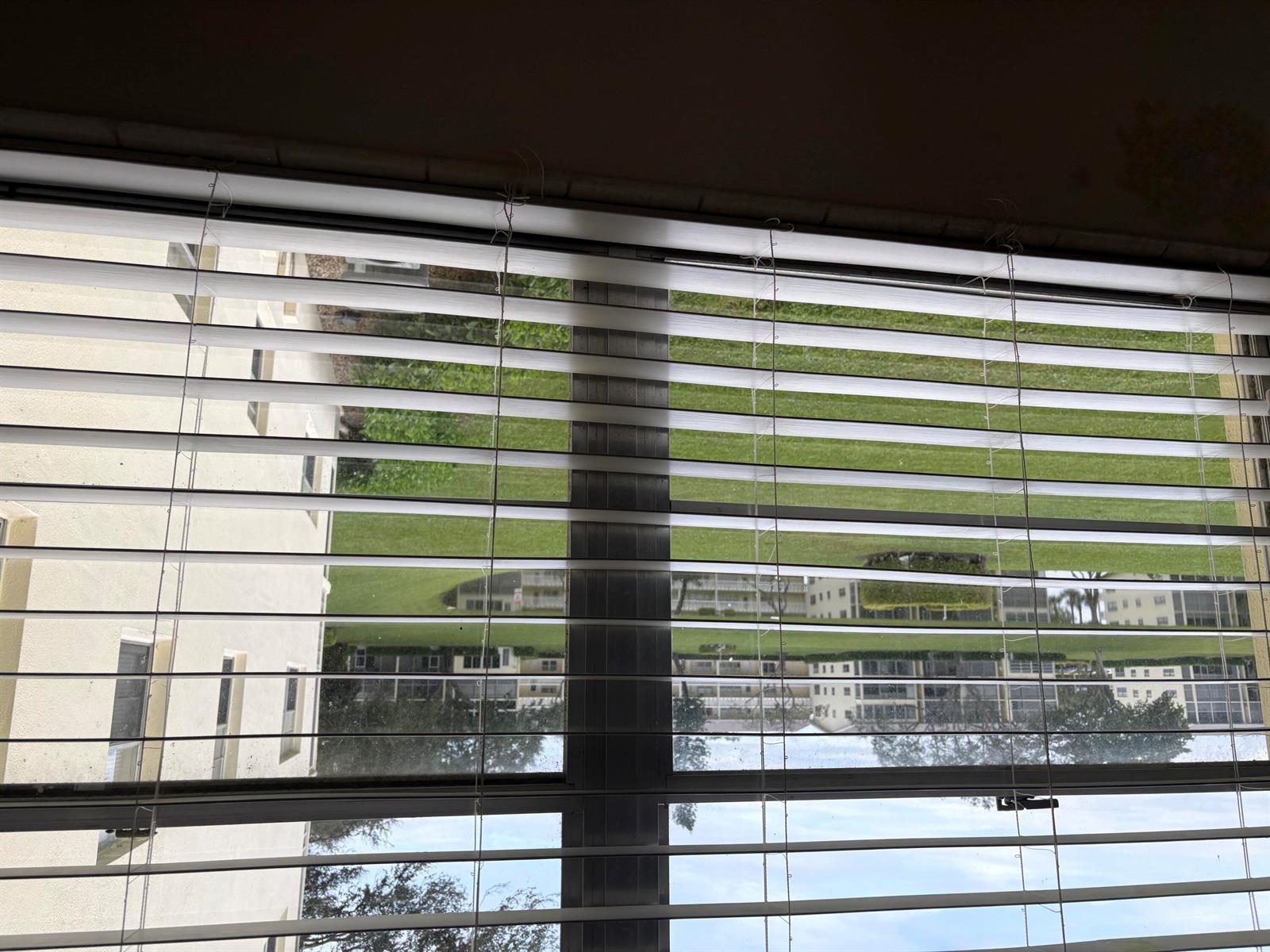 A view of a grassy lawn and apartment buildings seen through closed window blinds — 186 Dorset E, Boca Raton FL 33434, BOCA RATON, FL