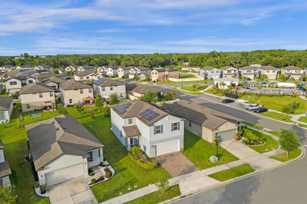 An aerial view shows suburban houses with solar panels and a nearby community pool — 3504 SOUTHERN CROSS LOOP, KISSIMMEE, FL