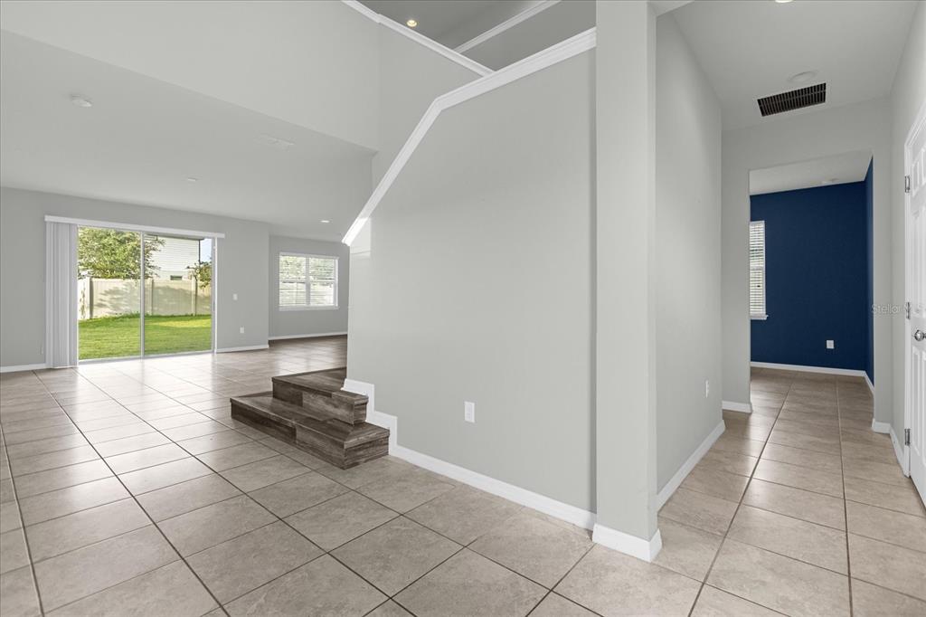 A light-filled foyer with tile flooring leads to a living area with wood-look stairs — 3504 SOUTHERN CROSS LOOP, KISSIMMEE, FL