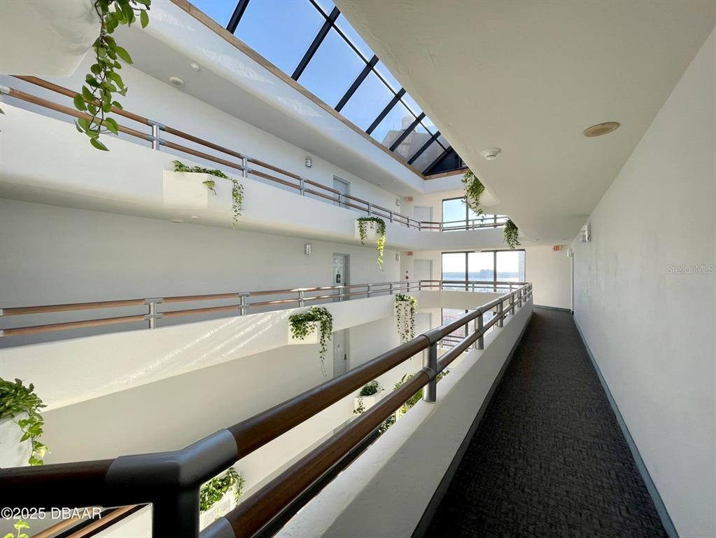 An indoor atrium hallway features multiple levels with wooden railings and a large skylight — 3023 S ATLANTIC AVENUE UNIT 8010, DAYTONA BEACH, FL