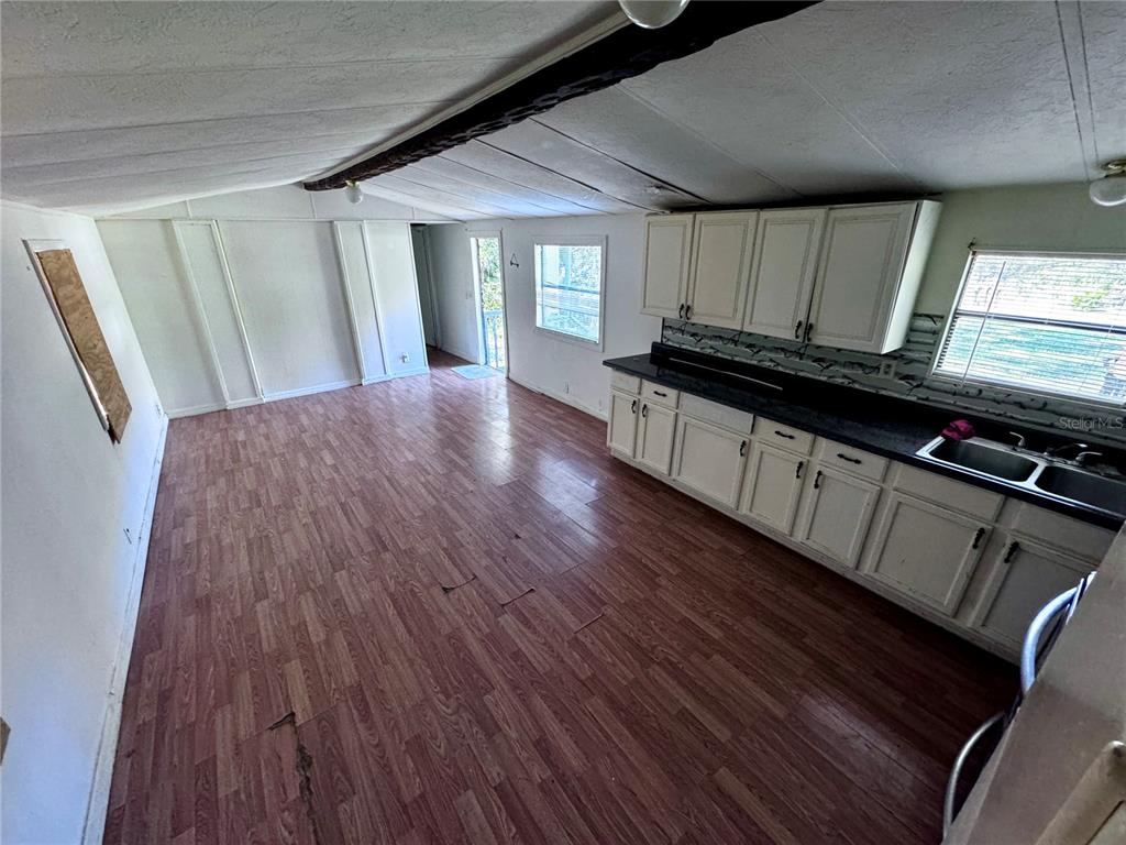 An open-concept kitchen and living area features wood-look flooring, white cabinets, and dark countertops — 13330 SW 9TH LANE, OCALA, FL