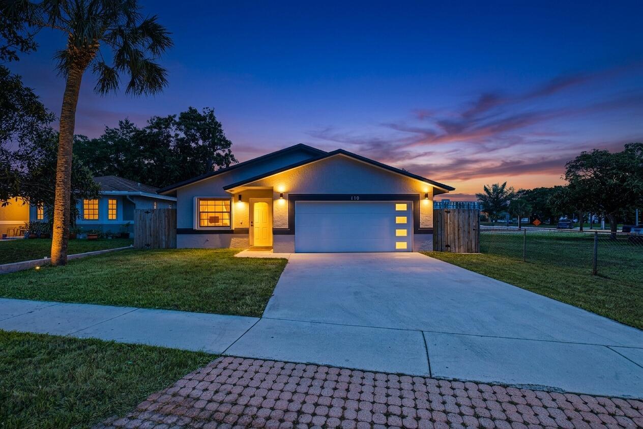 A single-story house with a white garage door and a paved driveway at twilight — 110 NW 6th Avenue, Dania Beach FL 33004, DANIA BEACH, FL