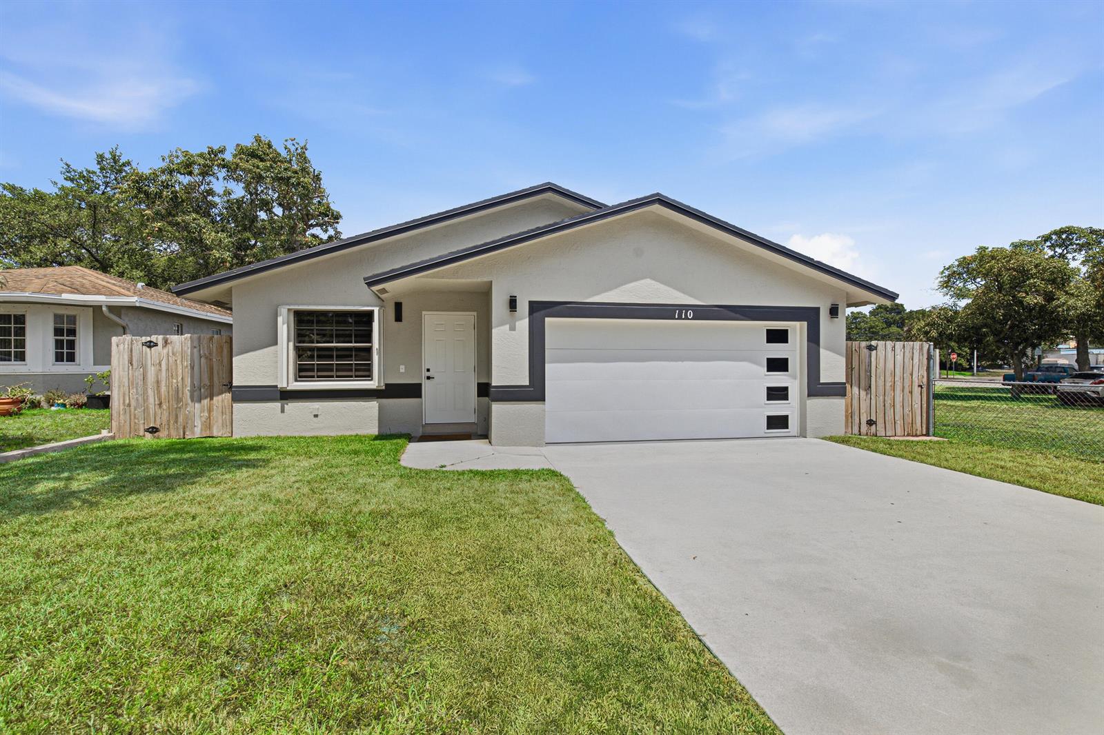 A single-story house with a white garage door, gray exterior walls, and a concrete driveway — 110 NW 6th Avenue, Dania Beach FL 33004, DANIA BEACH, FL