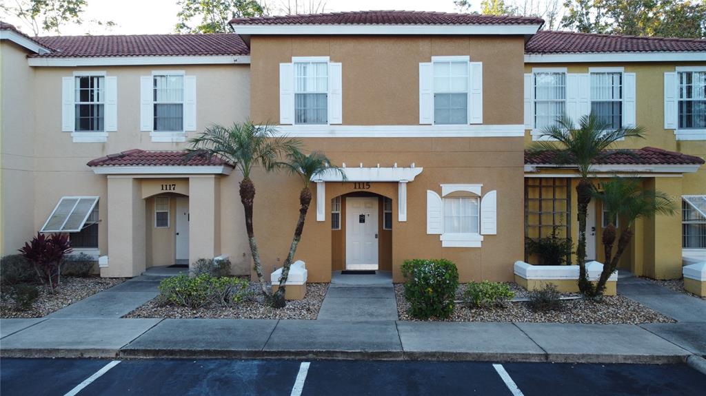 The exterior of a two-story townhouse complex features tan stucco walls and a tiled roof — 1115 PARK RIDGE CIRCLE, KISSIMMEE, FL