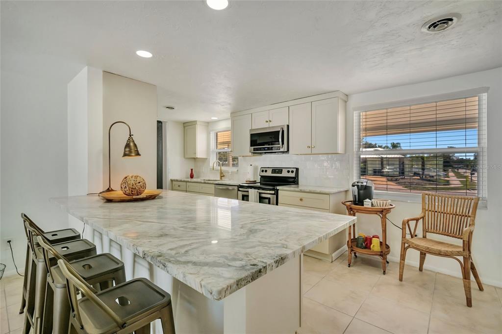 A kitchen features a large marble-topped island, white cabinetry, stainless steel appliances, and tile flooring — 6426 COLONIAL DRIVE, SARASOTA, FL