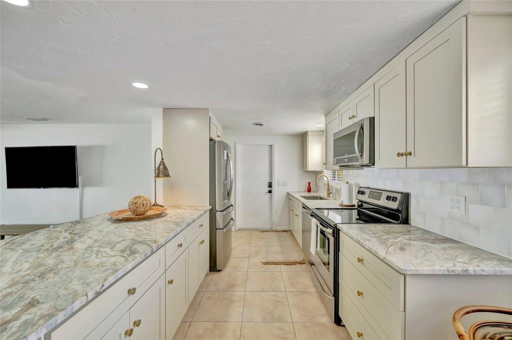 A kitchen features light-colored cabinets, marble-patterned countertops, stainless steel appliances, and tile flooring — 6426 COLONIAL DRIVE, SARASOTA, FL
