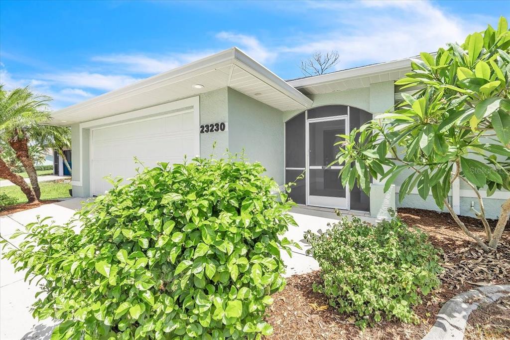 A pale green house exterior features a white garage door, a screened entryway, and landscaping — 23230 STELLING AVENUE, PORT CHARLOTTE, FL