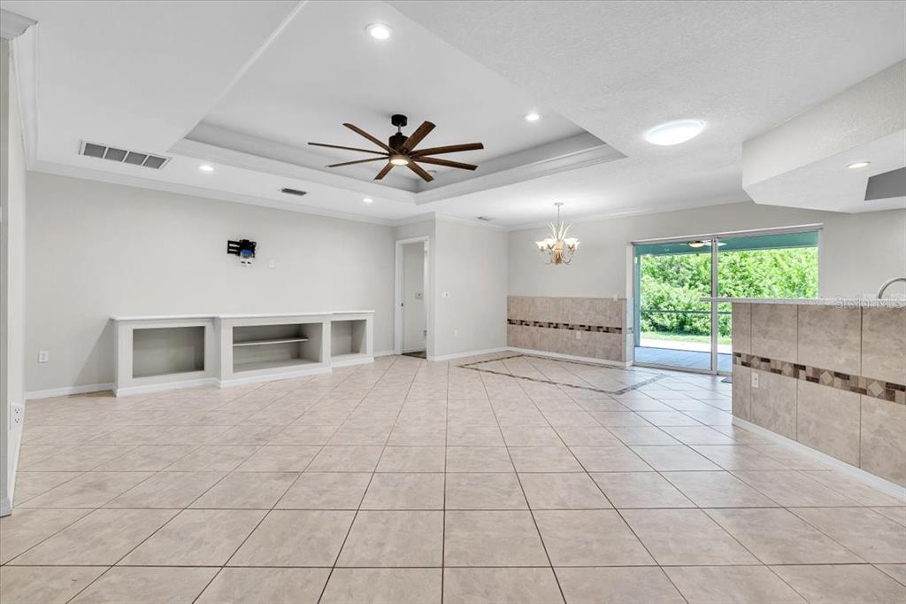 A spacious living area features tile flooring, a tray ceiling with a fan, and built-in shelving — 23230 STELLING AVENUE, PORT CHARLOTTE, FL