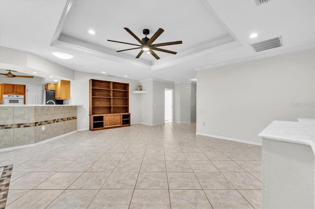 A spacious living area features tile flooring, a tray ceiling with a fan, and built-in shelving — 23230 STELLING AVENUE, PORT CHARLOTTE, FL