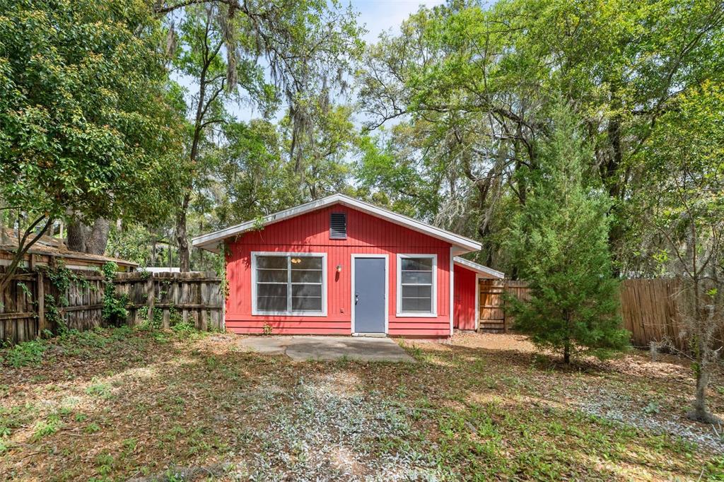 A small red detached building with a gray door sits in a wooded backyard — 615 NW 24TH AVENUE, GAINESVILLE, FL