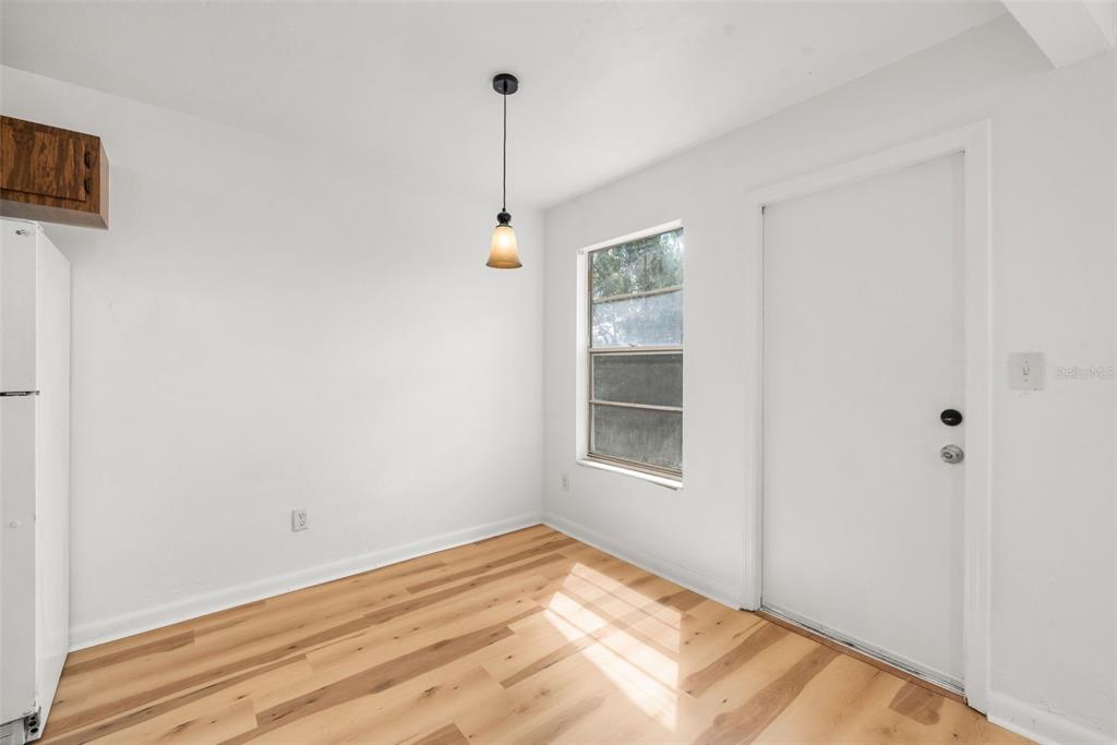 A bright, empty room features light wood-look flooring, white walls, a pendant light, and a door — 615 NW 24TH AVENUE, GAINESVILLE, FL