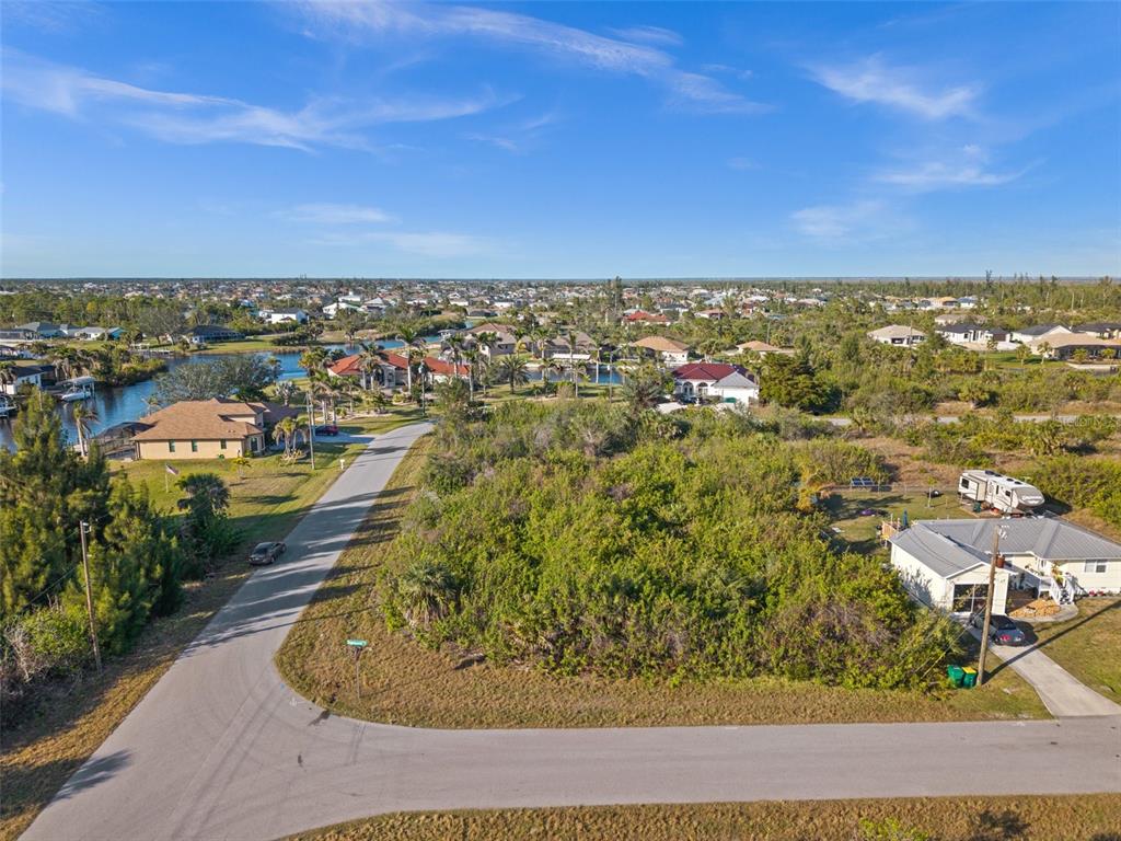 An aerial view shows a vacant, brush-covered lot situated between a road and a house — 10177 OWL HEAD CIRCLE, PORT CHARLOTTE, FL