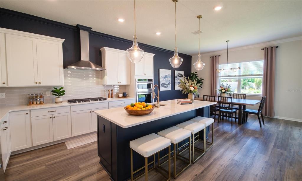 A modern kitchen features white cabinets, a dark blue island with bar stools, and dining area — 13360 PANAMA BEACH COURT, ORLANDO, FL