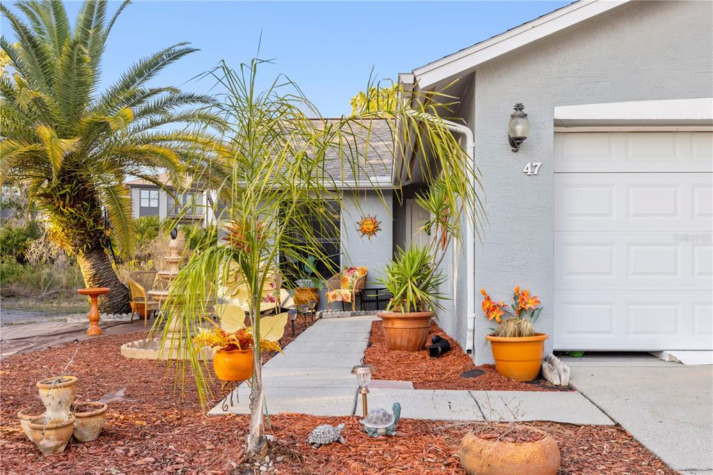 The exterior of a house features a concrete walkway, potted plants, and a garage door — 47 WOOD ACRE LANE, PALM COAST, FL