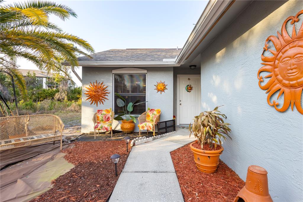 The exterior of a house features a concrete walkway, two chairs, and sun-themed wall decor — 47 WOOD ACRE LANE, PALM COAST, FL