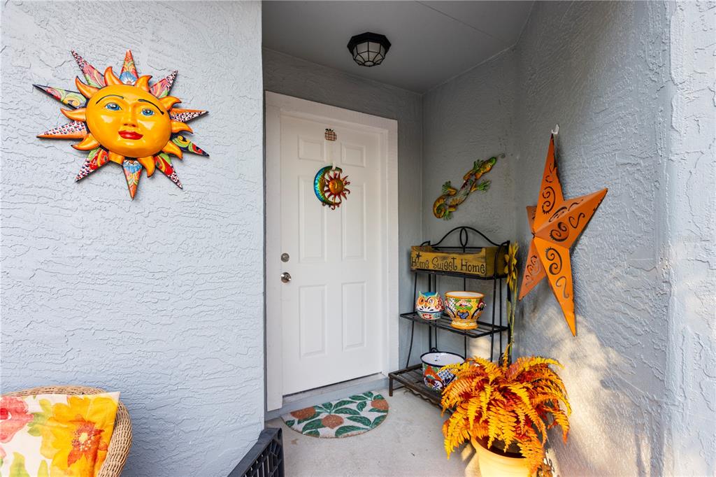 A front porch features a white door decorated with wall art, a plant stand, and a fern — 47 WOOD ACRE LANE, PALM COAST, FL