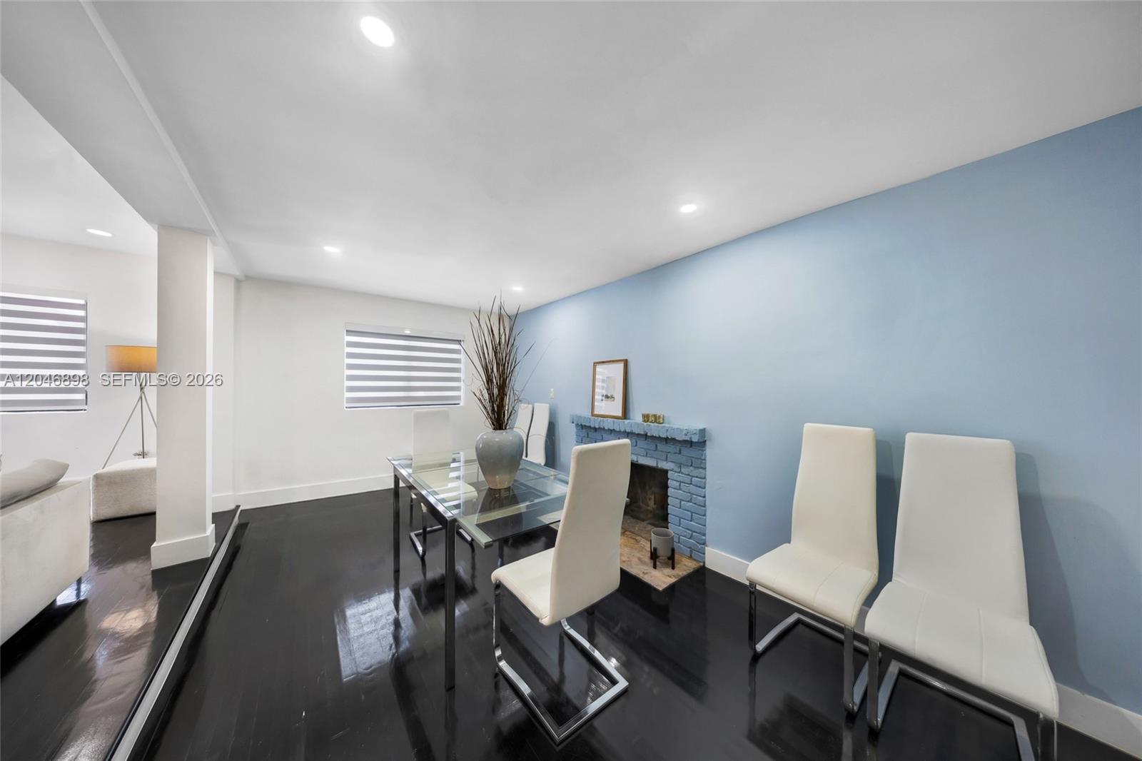 A dining room features a glass table, white chairs, a blue brick fireplace, and dark flooring — 6541 SW 18th St, West Miami FL 33155, WEST MIAMI, FL