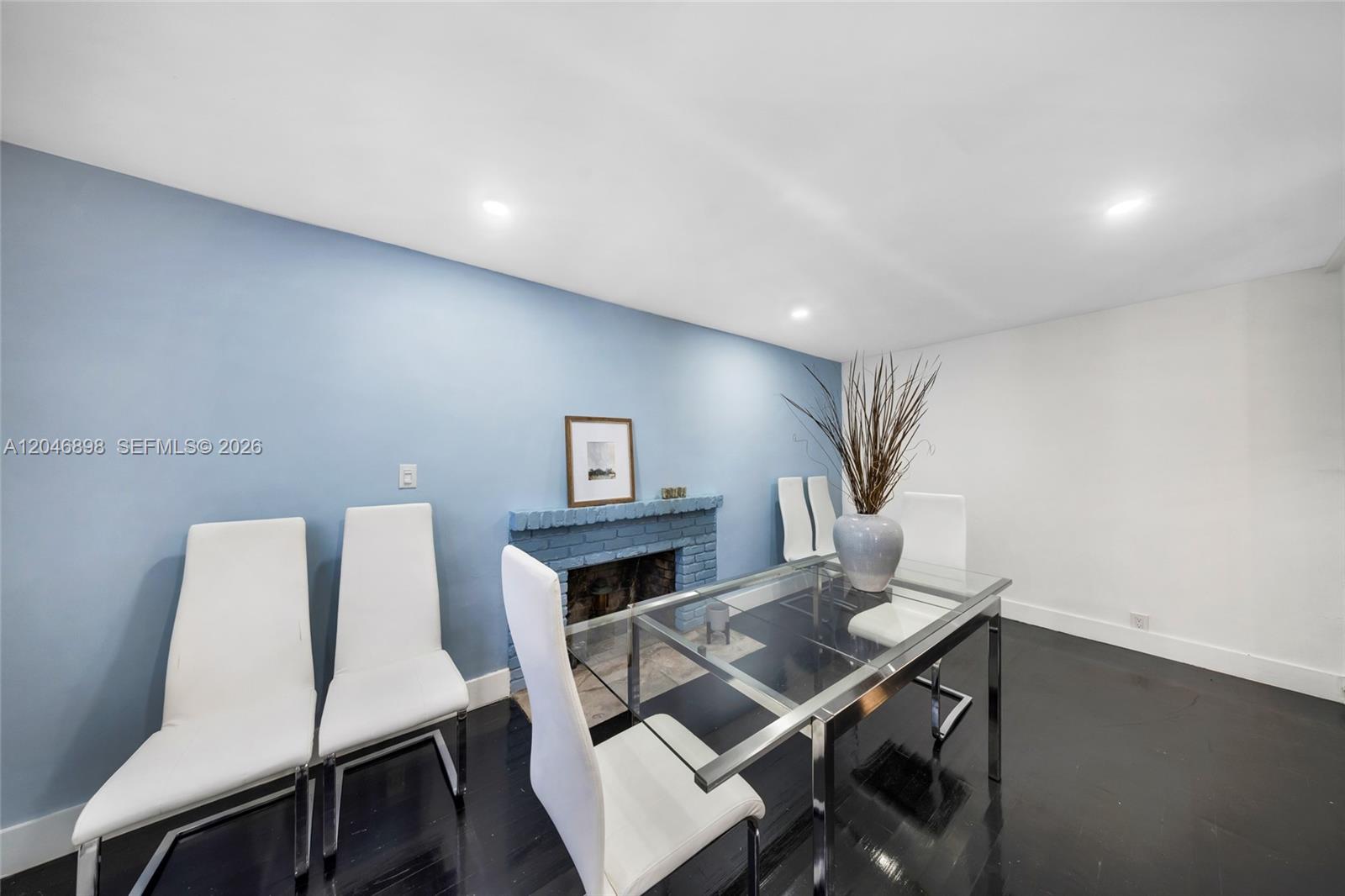 A dining room features a glass table, white chairs, a blue fireplace, and dark flooring — 6541 SW 18th St, West Miami FL 33155, WEST MIAMI, FL