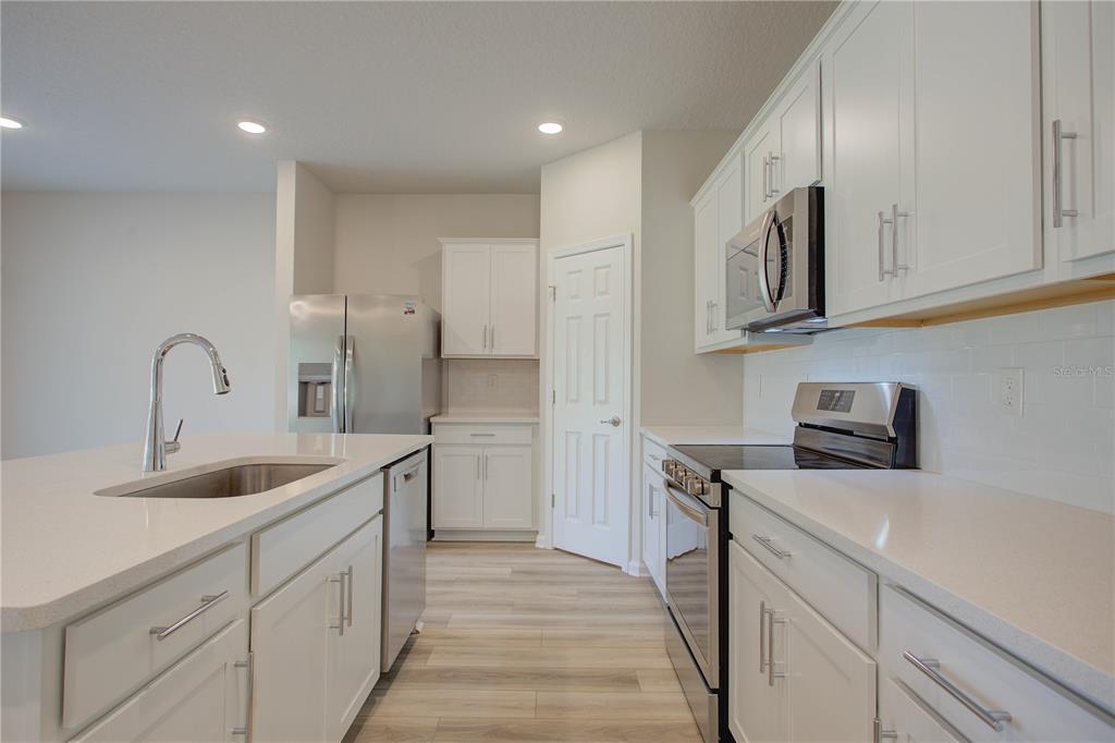 A modern kitchen features white cabinetry, stainless steel appliances, and a central island with sink — 10 FRENEAU LANE, PALM COAST, FL