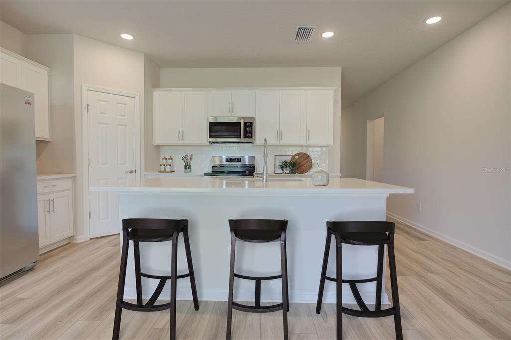 A kitchen features white cabinetry, a central island with three stools, and light wood flooring — 10 FRENEAU LANE, PALM COAST, FL