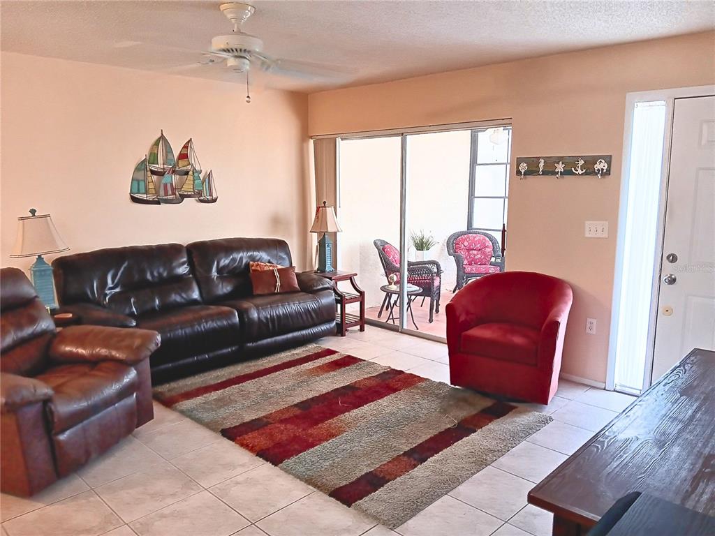 A living room features tile flooring, a brown leather sofa, a red armchair, and a rug — 8150 BRADDOCK CIRCLE UNIT 3, PORT RICHEY, FL