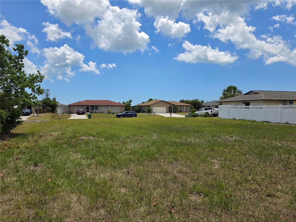 A vacant grassy lot sits in front of several suburban houses under a blue sky — 193 ANNAPOLIS LANE, ROTONDA WEST, FL