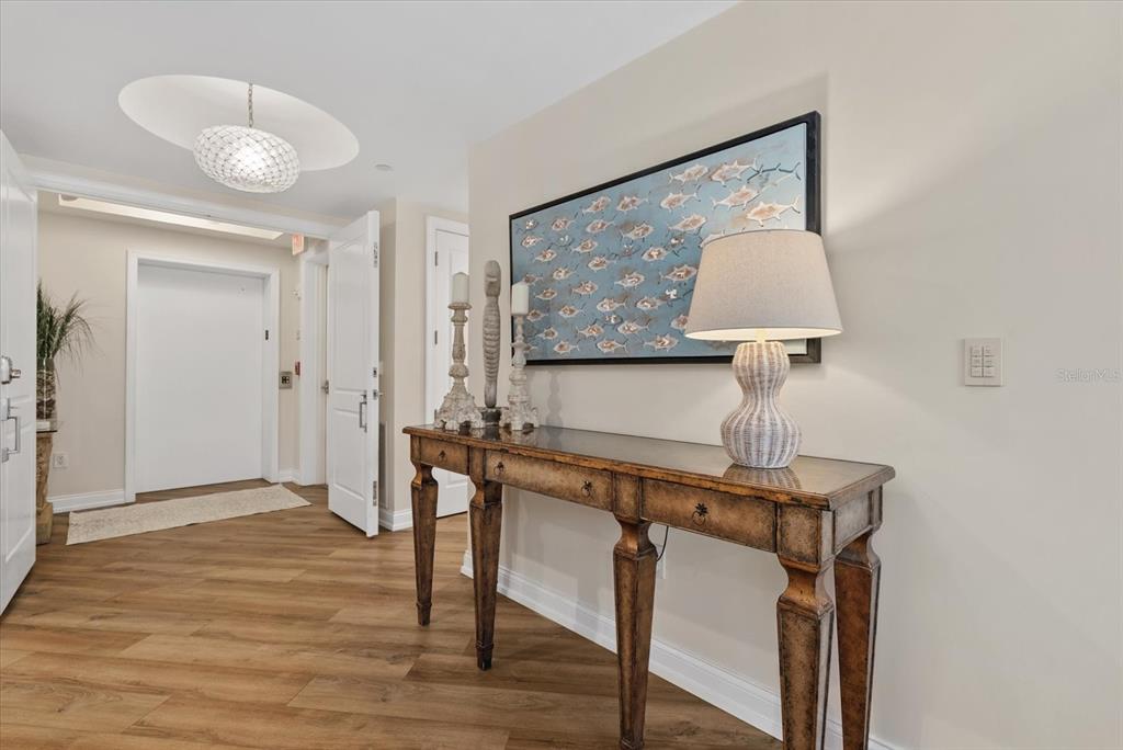 A hallway features wood-look flooring, a console table with a lamp, and framed fish artwork — 128 GOLDEN GATE POINT UNIT 202A, SARASOTA, FL