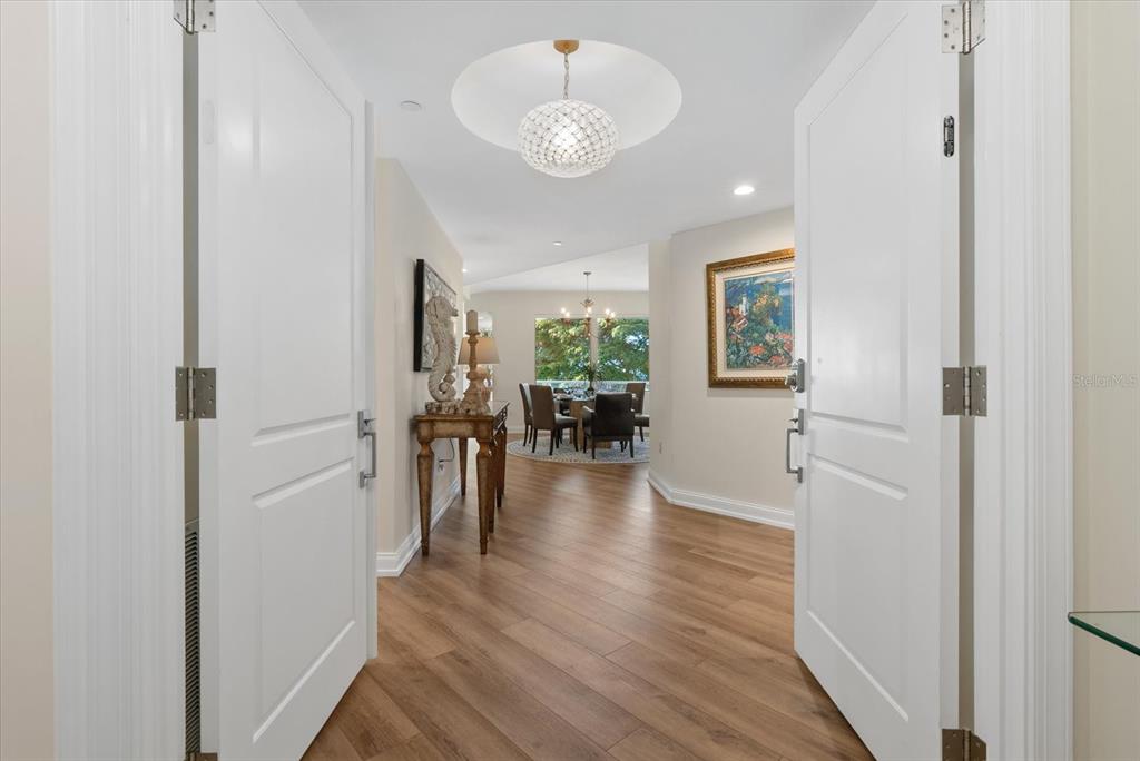 A wide-angle view of a foyer leading into a dining room with wood-look flooring — 128 GOLDEN GATE POINT UNIT 202A, SARASOTA, FL