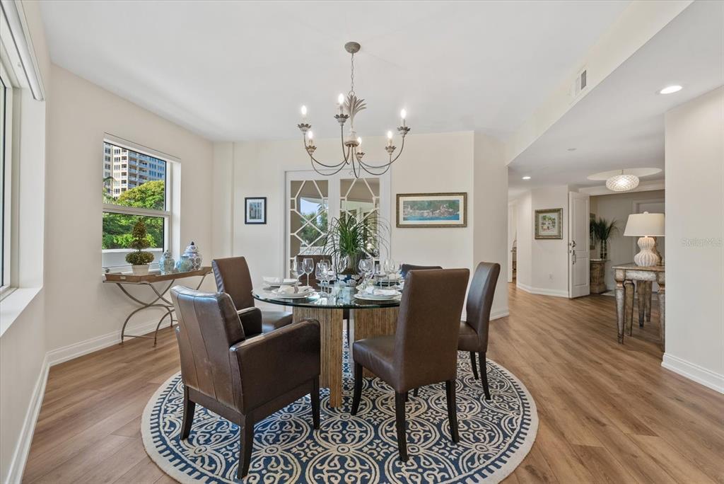A dining room features a glass-topped table, leather chairs, a chandelier, and wood-look flooring — 128 GOLDEN GATE POINT UNIT 202A, SARASOTA, FL