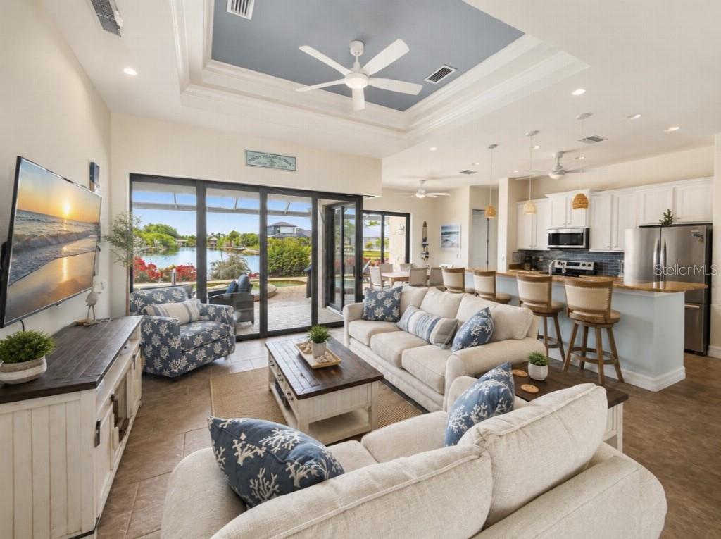 A living room with a tray ceiling, beige sofas, and sliding doors overlooking a lake — 15452 ALSASK CIRCLE, PORT CHARLOTTE, FL