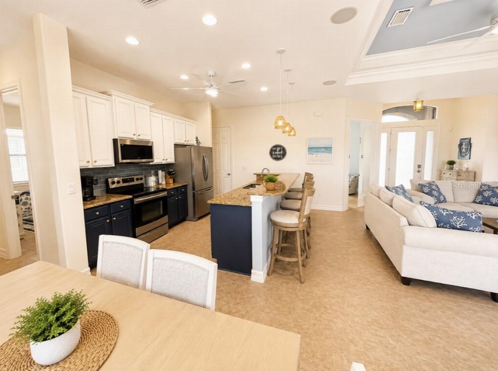 An open-concept kitchen features white upper cabinets, dark blue lower cabinets, and a granite island — 15452 ALSASK CIRCLE, PORT CHARLOTTE, FL