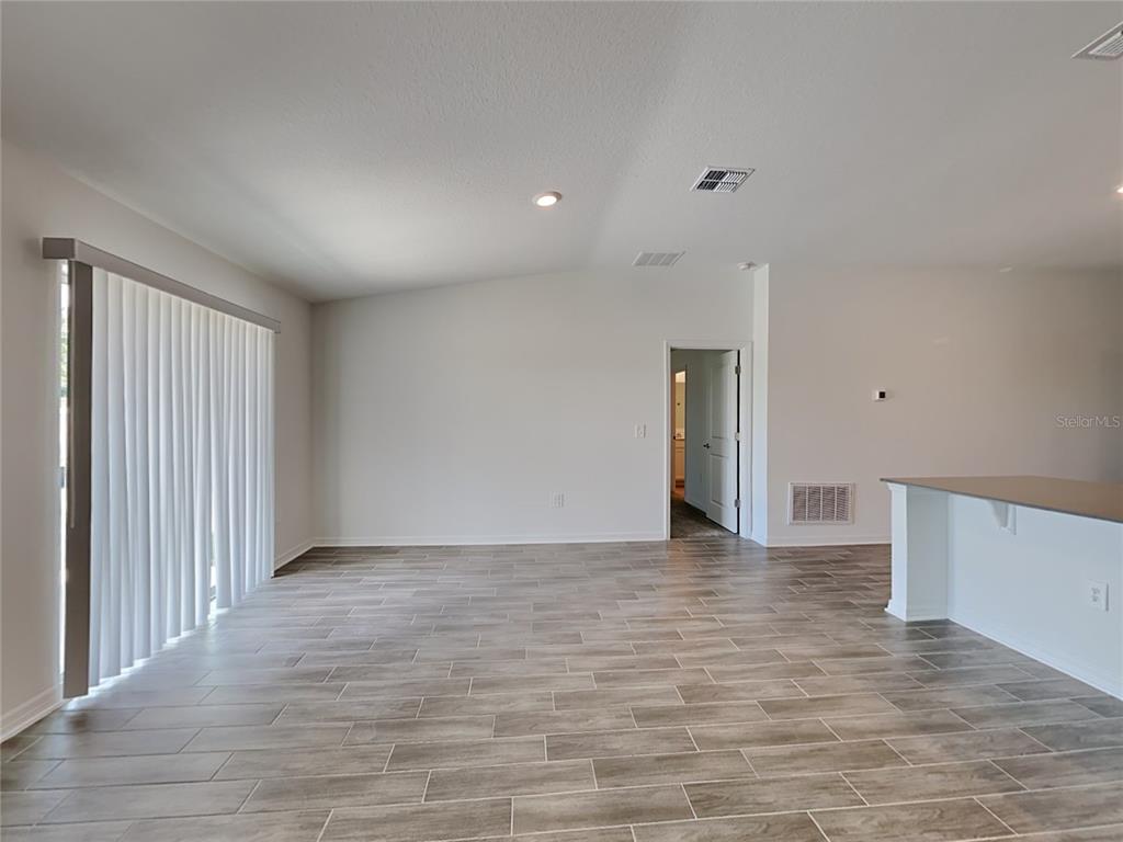 An empty room features light-colored walls, wood-look tile flooring, and a sliding glass door — 301 PIAVE STREET, HAINES CITY, FL