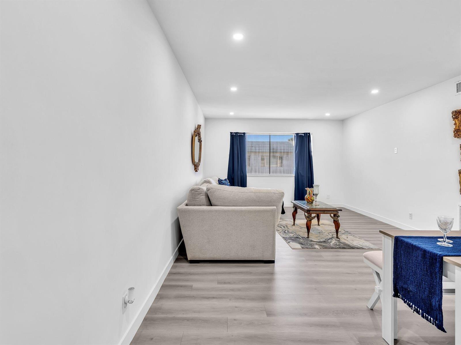 A living room features light wood-look flooring, a beige sofa, and dark blue curtains — 330 S Cypress Road # 628, Pompano Beach FL 33060, POMPANO BEACH, FL