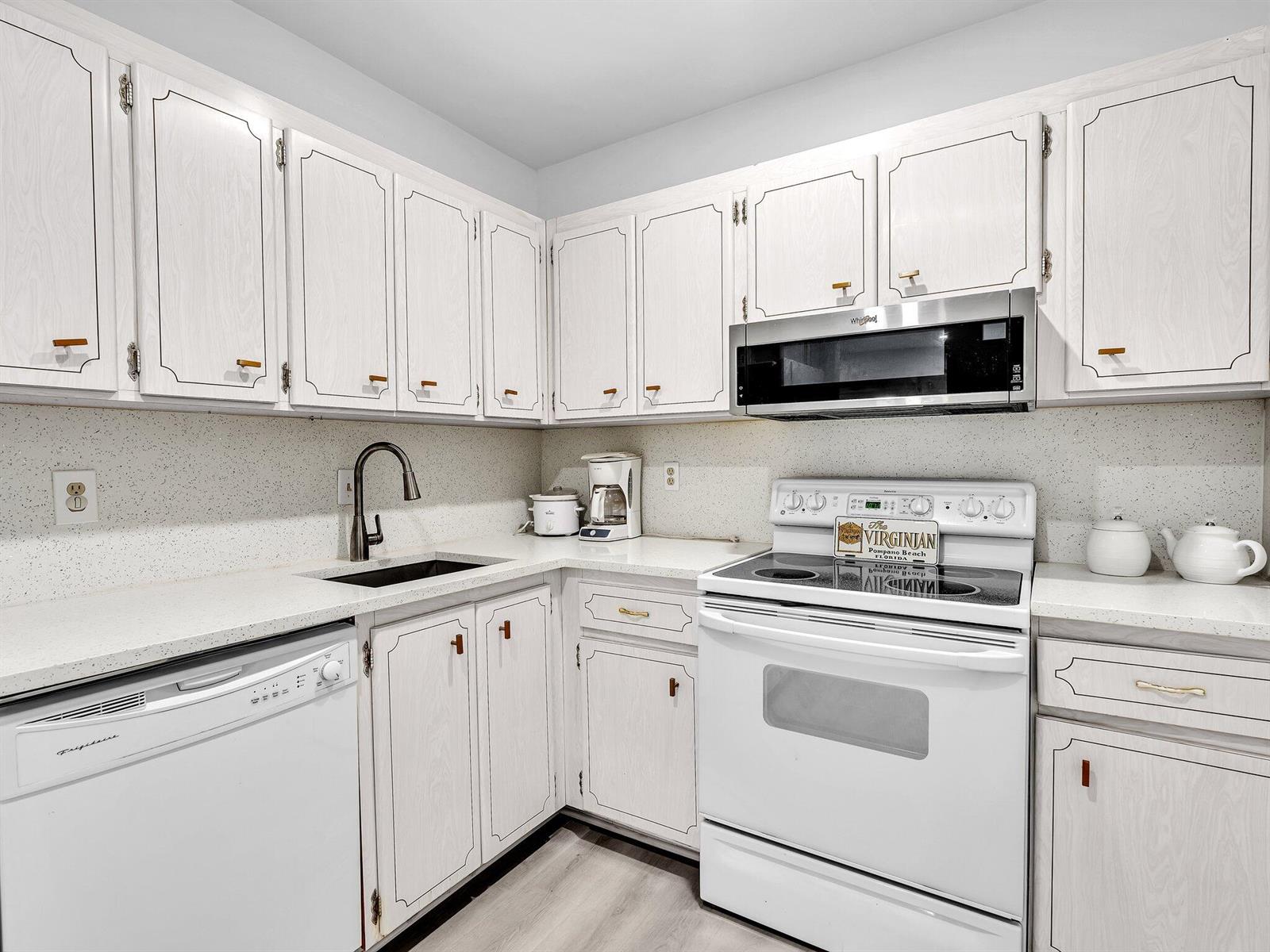 A kitchen features white cabinets, a white stove, a microwave, and a black sink — 330 S Cypress Road # 628, Pompano Beach FL 33060, POMPANO BEACH, FL