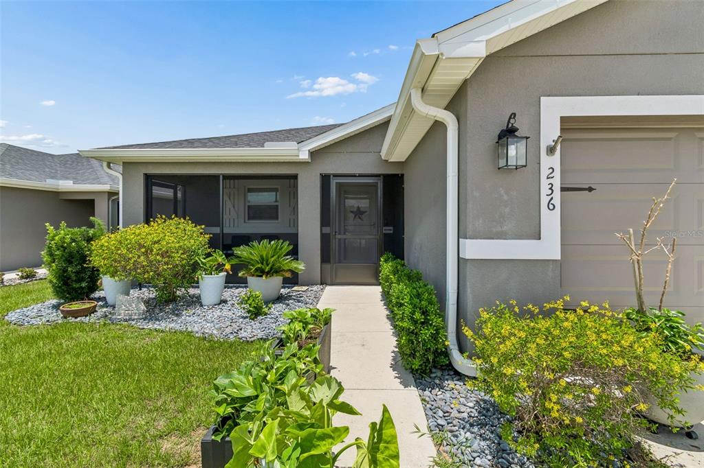 The exterior of a gray house features a screened entryway, a garage, and landscaped gardens — 236 FOXTAIL LOOP, DAVENPORT, FL