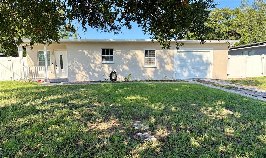 A single-story house with a white garage door, front door, and lawn under a tree — 706 ROMANO AVENUE, ORLANDO, FL