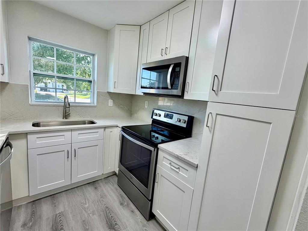 A kitchen features white shaker cabinets, stainless steel appliances, and light countertops with gray flooring — 706 ROMANO AVENUE, ORLANDO, FL