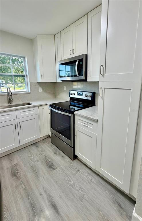 A kitchen features white cabinets, stainless steel appliances, and light-toned wood-look flooring — 706 ROMANO AVENUE, ORLANDO, FL